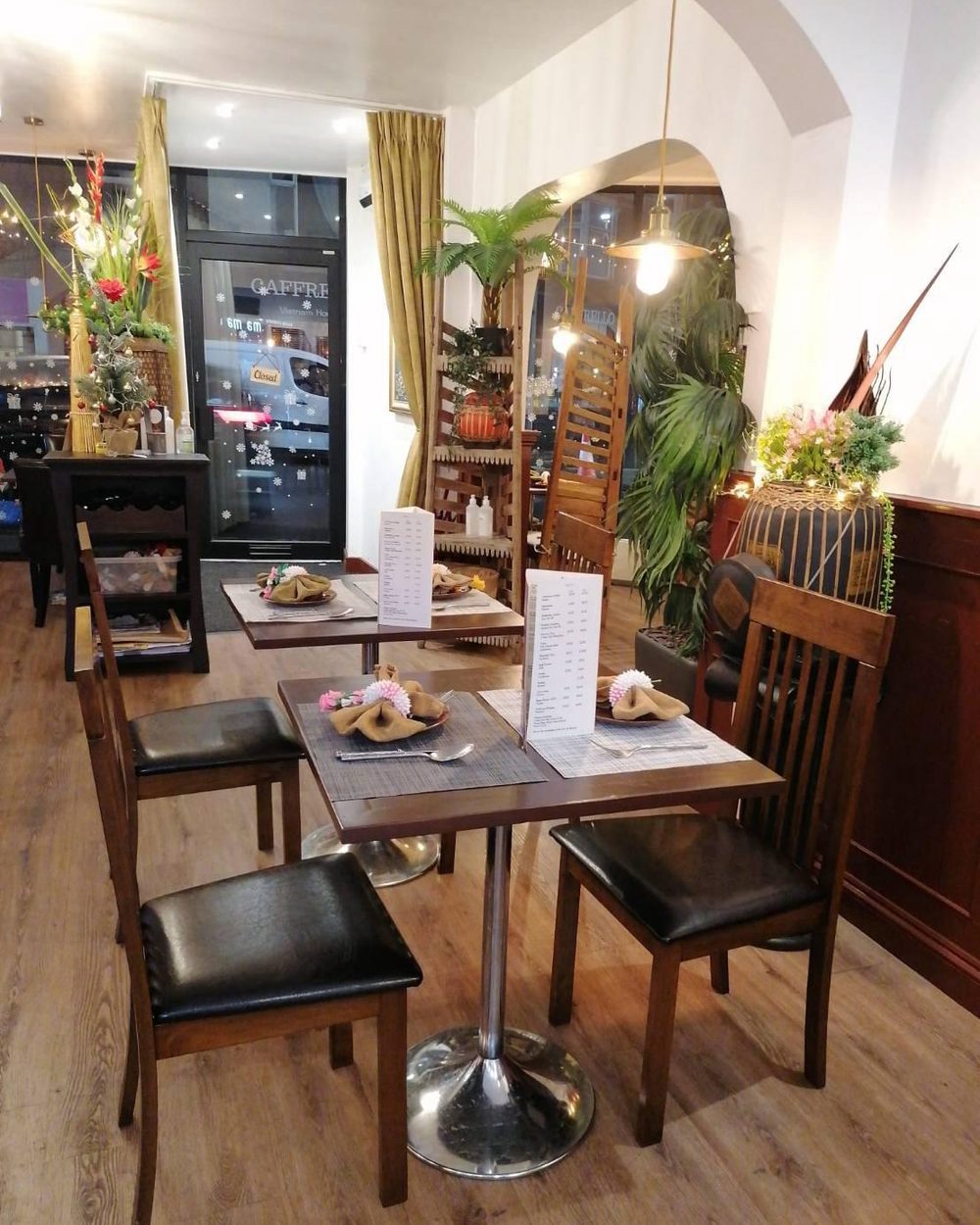 The dining room at Ma Ma Thai Newark, with dark wood tables, laid place settings and palms